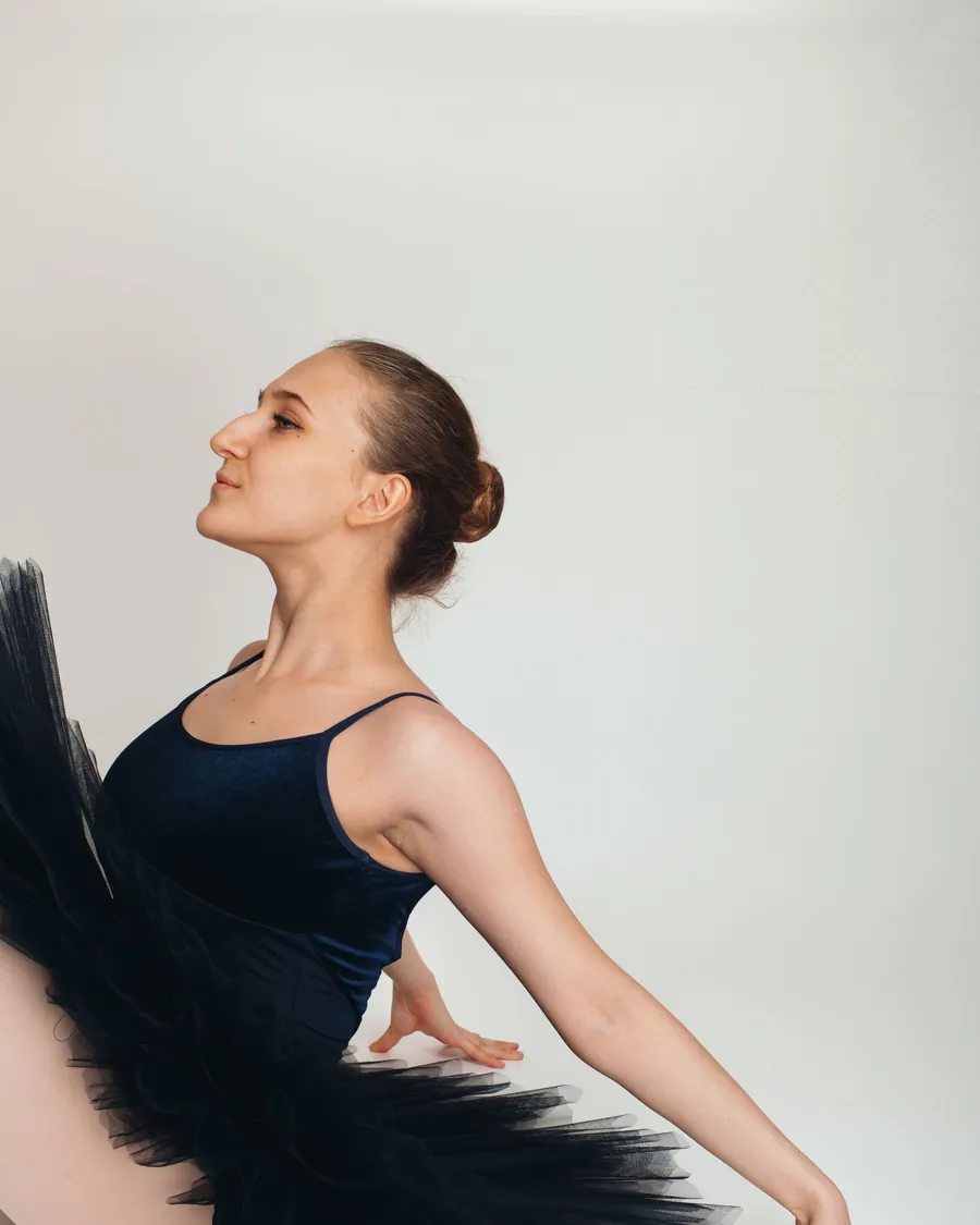 Bailarina de clásico en arabesque con tutú negro contra pared clara