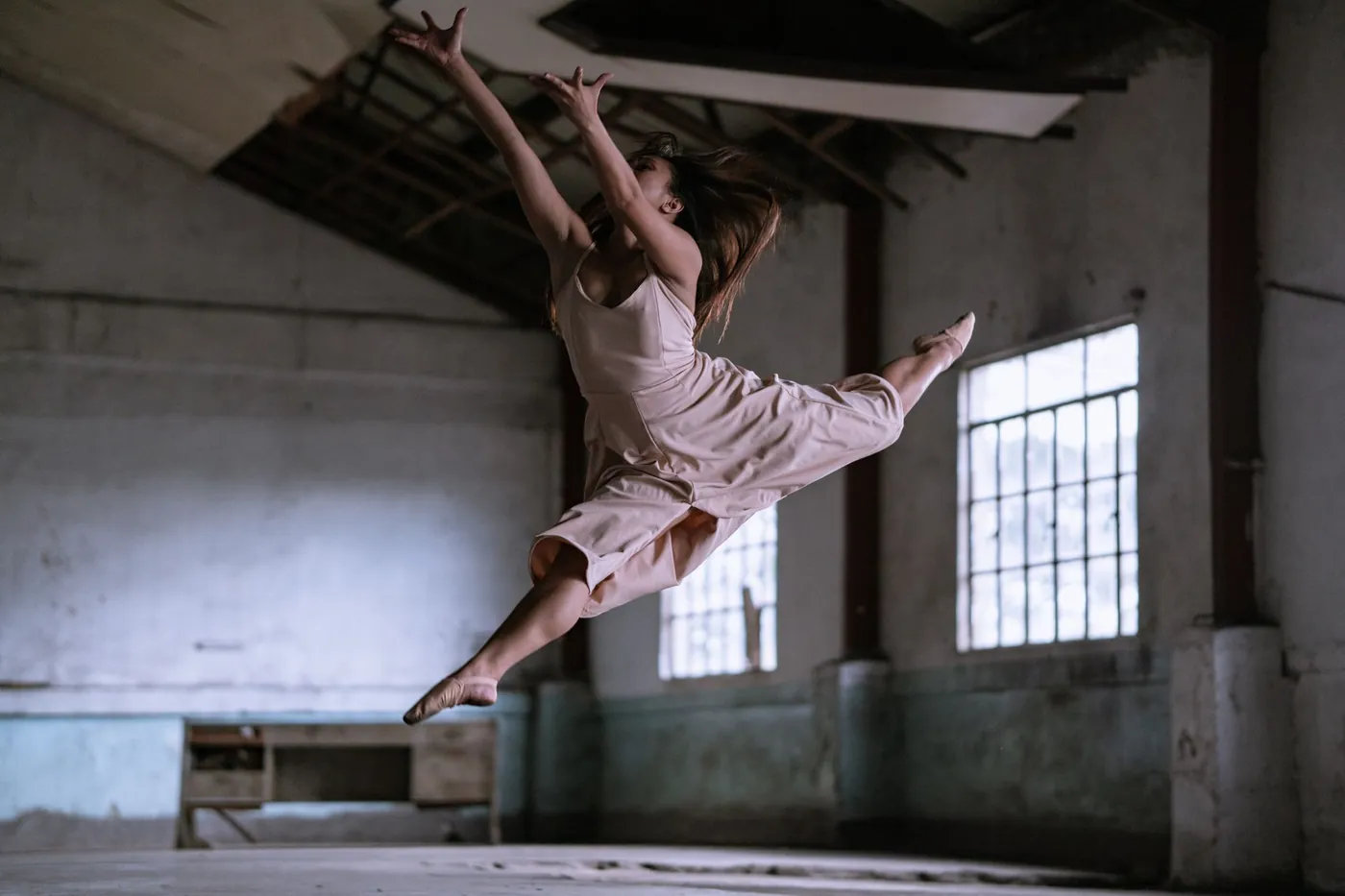 Bailarina en salto amplio dentro de una sala de ensayo con ventanales