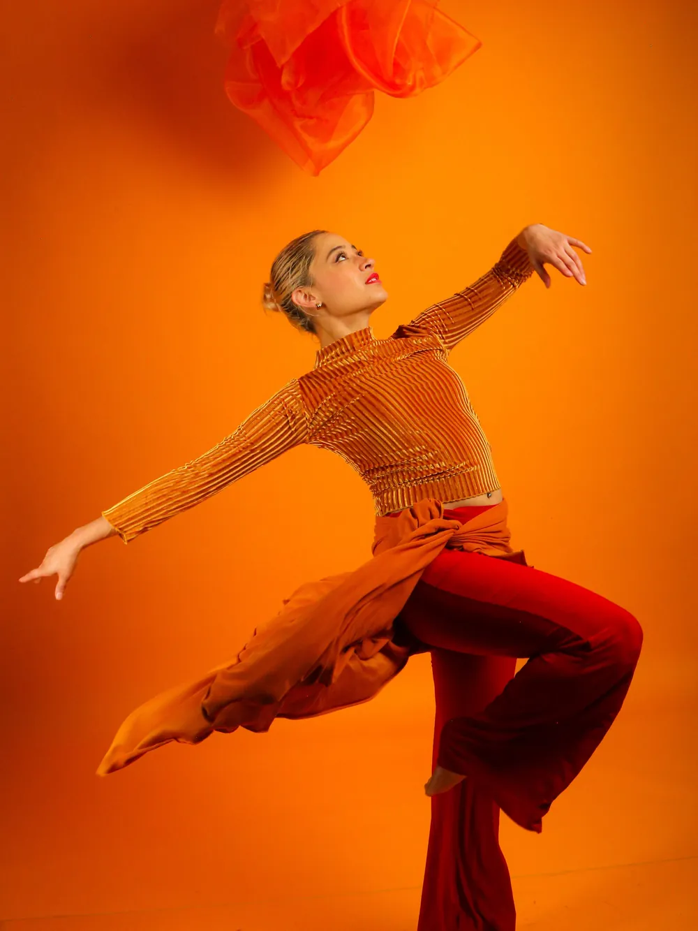 Bailarina de jazz en plena extensión, brazos abiertos, sobre fondo naranja